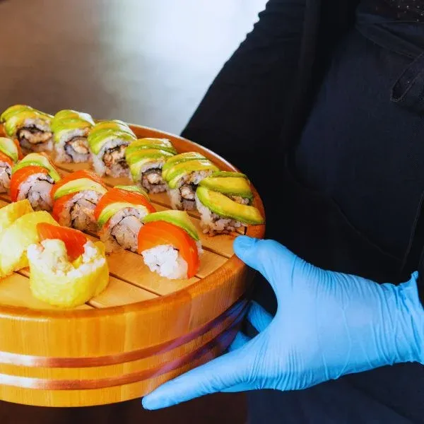 Plateau de sushis makis au saumon et à l'avocat tenu par une main gantée
